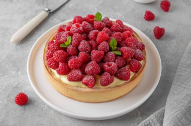 Kremalı vanilya kremalı lezzetli ahududu tartı, gri beton arka planda beyaz bir tabakta pudra şekeri serpiştirilmiş. Yaz tatlısı