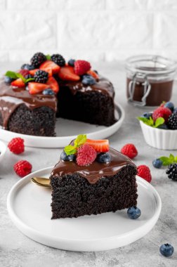 Çikolata kaplı lezzetli çikolatalı pasta ve gri beton arka planda beyaz bir tabakta taze meyveler.