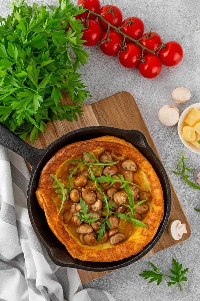 stock image Savory Dutch baby pancake with cheese, fried mushrooms and arugula in cast iron pan on a concrete background. Vegetarian breakfast