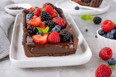 Taze böğürtlenli çikolatalı tart ve gri arka plandaki tabağın üstünde nane şekeri. Yaz tatlısı. Boşluğu kopyala