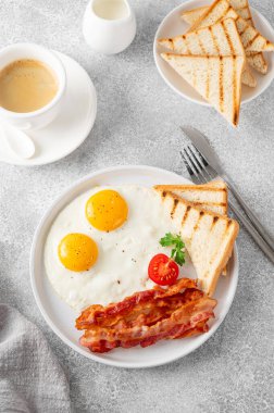 Yumurtalı kahvaltı, pastırma ve tostlar beyaz tabakta ve arka planda bir fincan kahveyle. Üst görünüm, seçici odak