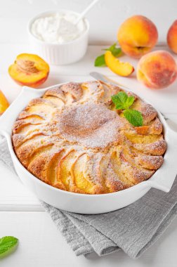 Beyaz ahşap zemin üzerinde beyaz seramik fırın şeklinde nefis şeftalili turta. Yaz pastası. Seçici odak, boşluğu kopyala