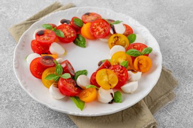 Kiraz domatesli Caprese salatası, mini mozzarella ve beyaz tabakta balzamik sirkeli taze fesleğen. Sağlıklı vejetaryen yemeği
