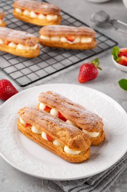 Krema ve taze çilek serpiştirilmiş ekkler gri beton arka planda üzerine pudra şekeri serpiştirilmiş.