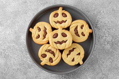 Cadılar Bayramı balkabağı şekilli sandviç kurabiyeleri ve kremalı gri bir tabakta beton bir arka planda süt. Fener kurabiyeleri. Üst görünüm