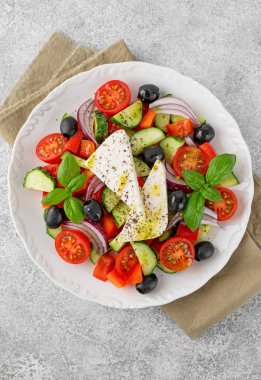 Yunan salatası taze meyve suyu, feta peyniri, otlar ve zeytinler beyaz bir tabakta açık beton arka planda. Sağlıklı yiyecekler. Boşluğu kopyala, üst görünüm