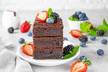 Çikolata kaplı bir yığın browni, gri beton arka planda beyaz bir tabakta taze böğürtlen ve nane yaprakları. Tatlı nefis.