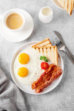 Yumurtalı kahvaltı, pastırma ve tostlar beyaz tabakta ve arka planda bir fincan kahveyle. Üst görünüm, seçici odak