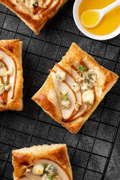 stock image Mini tarts with puff pastry, pieces of pear, blue cheese, walnuts and honey on a concrete background. Top view