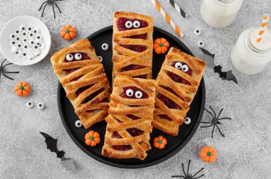 Halloween mummies pies with cherry filling and sugar eyes on a gray concrete background. Funny food idea. Holiday dessert. Top view clipart