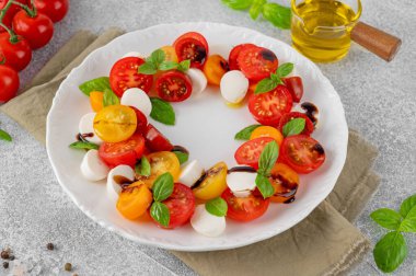 Kiraz domatesli Caprese salatası, mini mozzarella ve beyaz tabakta balzamik sirkeli taze fesleğen. Sağlıklı vejetaryen yemeği
