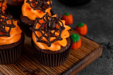 Cadılar Bayramı çikolatalı kekler, üzerinde turuncu krema ve koyu arkaplanda çikolata örümcek ağı var. Bayramlık tatlı. Komik yemek fikri. Boşluğu kopyala