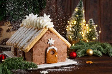 Üzerine pudra şekeri serpiştirilmiş beyaz bir tabakta ev şeklinde Noel çikolatalı pasta. Şenlikli tatlı.