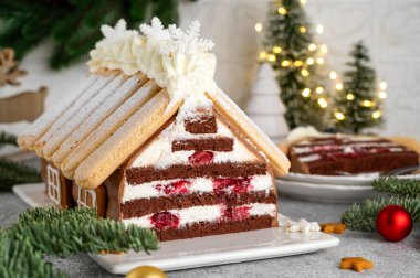 Üzerine pudra şekeri serpiştirilmiş beyaz bir tabakta ev şeklinde Noel çikolatalı pasta. Şenlikli tatlı.