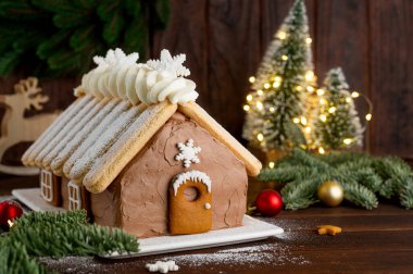 Üzerine pudra şekeri serpiştirilmiş beyaz bir tabakta ev şeklinde Noel çikolatalı pasta. Şenlikli tatlı.