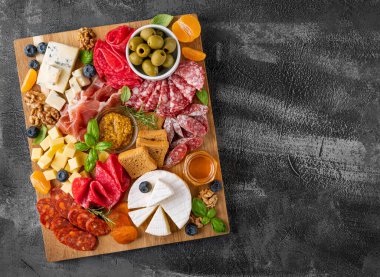 Çeşitli peynirli Charcuterie tahtası, salam, korizzo, prosciutto, bal, üzüm, fındık, zeytin, ekmek, yaban mersini ve koyu betondan yapılmış taze otlar. Şenlikli bir atıştırmalık