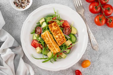 Salad with grilled halloumi cheese, tomatoes, avocado, cucumber and olive oil on a concrete background. Healthy food. Top view. clipart