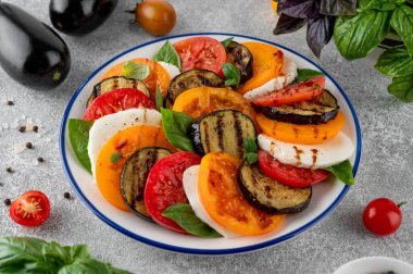 Balzamik soslu patlıcan caprese salatası ve gri bir arka planda taze fesleğen. Vejetaryen yemeği. Üst görünüm, alanı kopyala