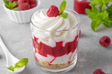 Krem şantili ahududu tatlısı, çilek sosu, kurabiye kırıntıları ve gri beton arka planda bir bardaktaki nane yaprakları. Yaz diyeti tatlısı