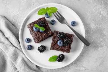 Çikolata kaplı brovniler, taze böğürtlenler ve nane yaprakları gri beton arka planda beyaz bir tabakta. Tatlı nefis.