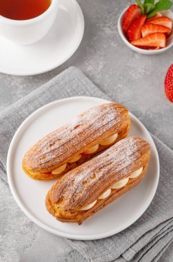 Krema ve taze çilek serpiştirilmiş ekkler gri beton arka planda üzerine pudra şekeri serpiştirilmiş.