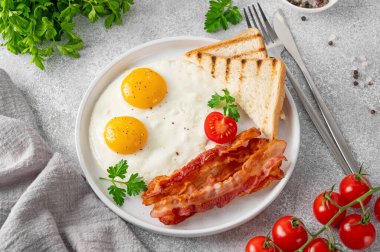 Yumurtalı kahvaltı, pastırma ve tostlar beyaz tabakta ve arka planda bir fincan kahveyle. Üst görünüm, seçici odak