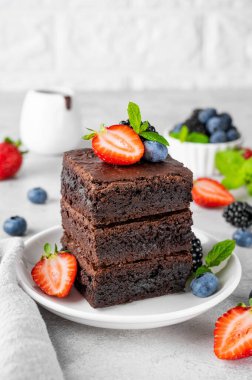 Çikolata kaplı bir yığın browni, gri beton arka planda beyaz bir tabakta taze böğürtlen ve nane yaprakları. Tatlı nefis.