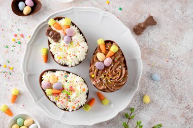 Paskalya tatlısı. Çikolatalı yumurtalar çikolata şekerleri ve şeker parçacıkları ile süslenmiş gri beton arka planda beyaz bir tabakta. Boşluğu kopyala