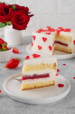 Sevgililer günü için küçük kırmızı kalpli vanilyalı çilekli pasta gri beton arka planda beyaz bir tabakta. Romantik pasta.