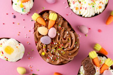 Paskalya tatlısı. Çikolatalı yumurtalar, çikolata şekerleri ve pembe arka planda şeker parçacıkları ile süslenmiş cheesecake dolgulu. Boşluğu kopyala, üst görünüm