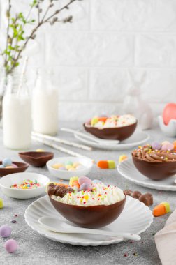 Paskalya tatlısı. Çikolatalı yumurtalar çikolata şekerleri ve şeker parçacıkları ile süslenmiş gri beton arka planda beyaz bir tabakta. Boşluğu kopyala