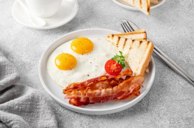 Yumurtalı kahvaltı, pastırma ve tostlar beyaz tabakta ve arka planda bir fincan kahveyle. Üst görünüm, seçici odak