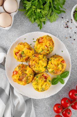 Yumurtalı kek ya da pastırma, peynir, sebze ve çimento kaplı beyaz bir tabakta otlu yumurta ısırığı. Sağlıklı kahvaltı.