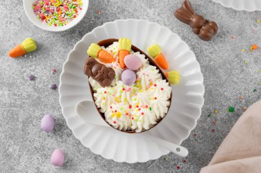 Paskalya tatlısı. Çikolatalı yumurtalar çikolata şekerleri ve şeker parçacıkları ile süslenmiş gri beton arka planda beyaz bir tabakta. Boşluğu kopyala