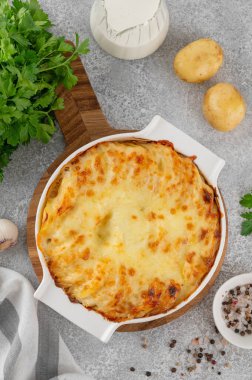 Krem, peynir ve sarımsaklı patatesli graten gri beton arka planda beyaz seramik bir form. Patates güveci. Üst görünüm, alanı kopyala