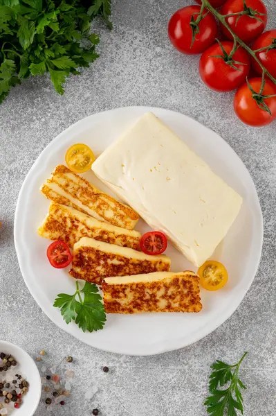 Kızarmış ve çiğ halloumi peyniri gri bir zeminde beyaz bir tabakta