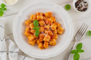 Domates soslu geleneksel patates gnocchi, parmesan peyniri ve beyaz ahşap arka planda taze fesleğen. İtalyan mutfağı. Üst görünüm, alanı kopyala