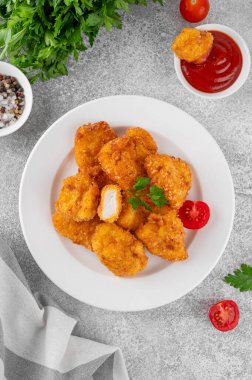 Beyaz tabakta ketçaplı çıtır tavuk külçeleri, gri beton arka planda.