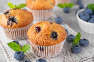 Tahta bir tahta üzerinde lezzetli yaban mersinli çörekler gri bir arka planda bir şişe süt, taze böğürtlen ve nane yapraklarıyla