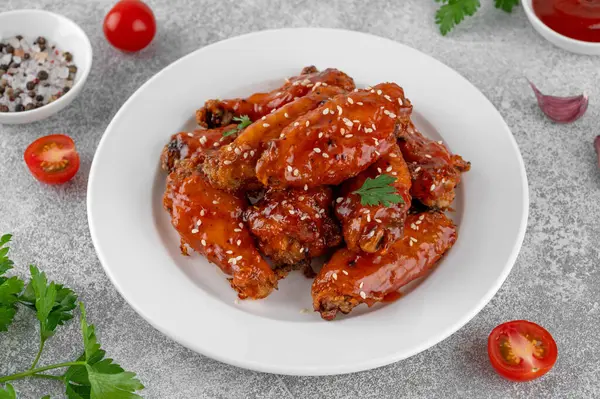 Tatlı acı biber soslu fırında tavuk kanadı ve beton bir zeminde beyaz bir tabakta susam tohumu. Üst görünüm, alanı kopyala