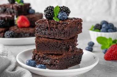 Çikolata kaplı bir yığın browni, gri beton arka planda beyaz bir tabakta taze böğürtlen ve nane yaprakları. Tatlı nefis.