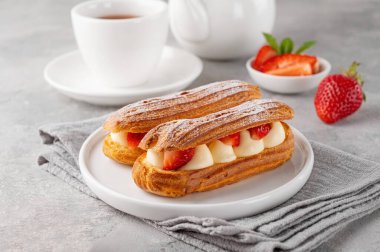 Krema ve taze çilek serpiştirilmiş ekkler gri beton arka planda üzerine pudra şekeri serpiştirilmiş.