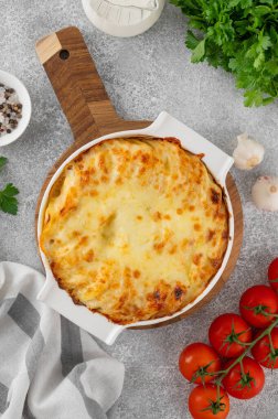 Krem, peynir ve sarımsaklı patatesli graten gri beton arka planda beyaz seramik bir form. Patates güveci. Üst görünüm, alanı kopyala