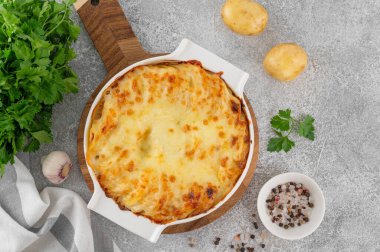 Krem, peynir ve sarımsaklı patatesli graten gri beton arka planda beyaz seramik bir form. Patates güveci. Üst görünüm, alanı kopyala