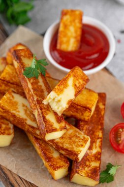 Beton zeminde ahşap bir tahtanın üzerinde domates soslu kızarmış halloumi peyniri çubukları.