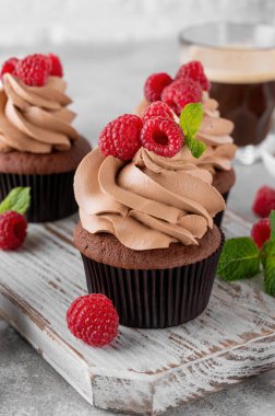 Kremalı çikolatalı kekler taze ahududu ve gri beton arka planda nane yapraklarıyla süslenmiş. Lezzetli bayram tatlısı.