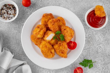 Beyaz tabakta ketçaplı çıtır tavuk külçeleri, gri beton arka planda.