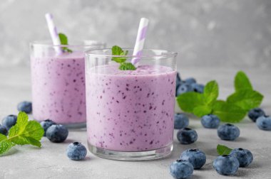 Yaban mersinli meyve suyu, muz, chia tohumu ve gri beton arka planda bir bardakta yoğurt. Sağlıklı yemek.