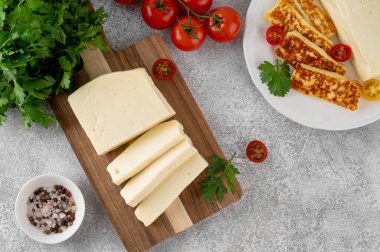 Ahşap bir tahtanın üzerinde beyaz peynir halloumi ve çimento kaplı otlar ve domatesler. Üst görünüm