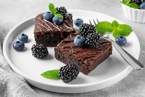 Çikolata kaplı brovniler, taze böğürtlenler ve nane yaprakları gri beton arka planda beyaz bir tabakta. Tatlı nefis.